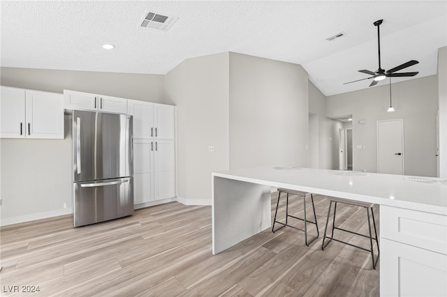 kitchen featuring a kitchen breakfast bar, vaulted ceiling, stainless steel fridge, light wood-type flooring, and white cabinetry