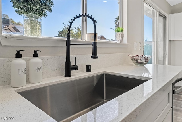 details with white cabinetry, light stone countertops, and sink