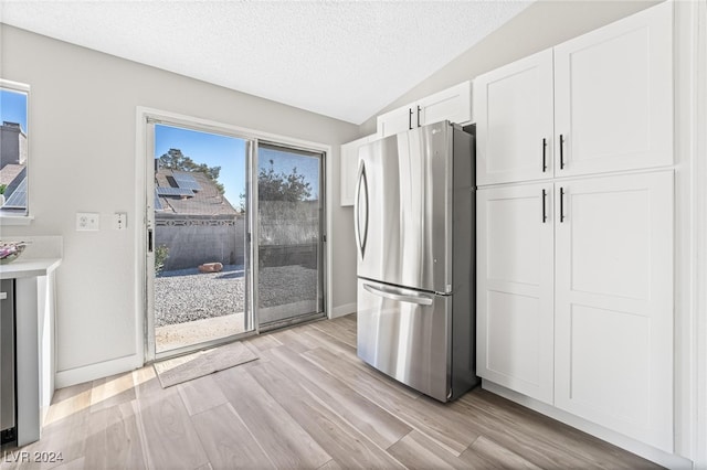 kitchen featuring lofted ceiling, light hardwood / wood-style flooring, a textured ceiling, white cabinetry, and stainless steel refrigerator