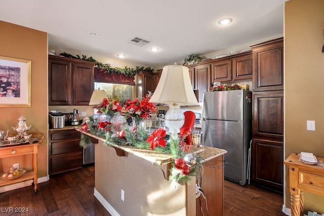 kitchen with stainless steel refrigerator, dark brown cabinets, a kitchen island, and dark wood-type flooring