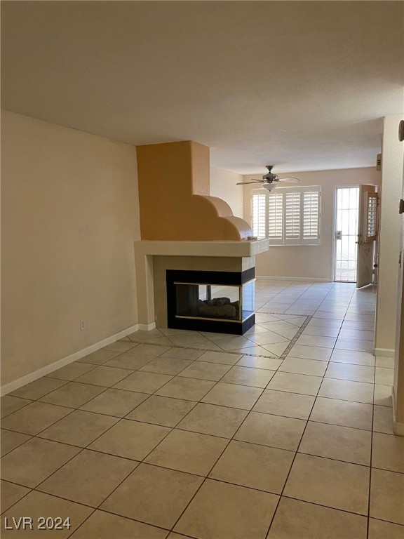 unfurnished living room with a multi sided fireplace, ceiling fan, and light tile patterned floors