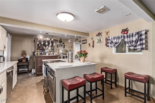 kitchen featuring visible vents, a breakfast bar, white cabinetry, appliances with stainless steel finishes, and light tile patterned flooring