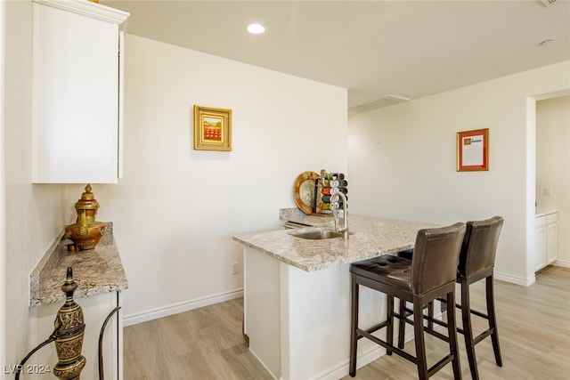 bar with white cabinets, light hardwood / wood-style floors, light stone countertops, and sink