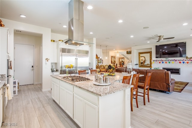 kitchen featuring a center island, light hardwood / wood-style flooring, light stone counters, island exhaust hood, and stainless steel appliances