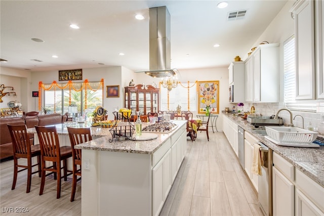 kitchen with a kitchen island, light stone countertops, island exhaust hood, and light hardwood / wood-style flooring