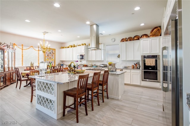 kitchen featuring appliances with stainless steel finishes, a kitchen breakfast bar, ventilation hood, decorative light fixtures, and an island with sink