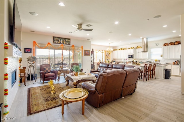 living room with light hardwood / wood-style flooring, a healthy amount of sunlight, and ceiling fan with notable chandelier