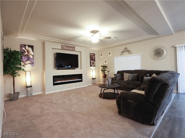 carpeted living room with a raised ceiling and ceiling fan