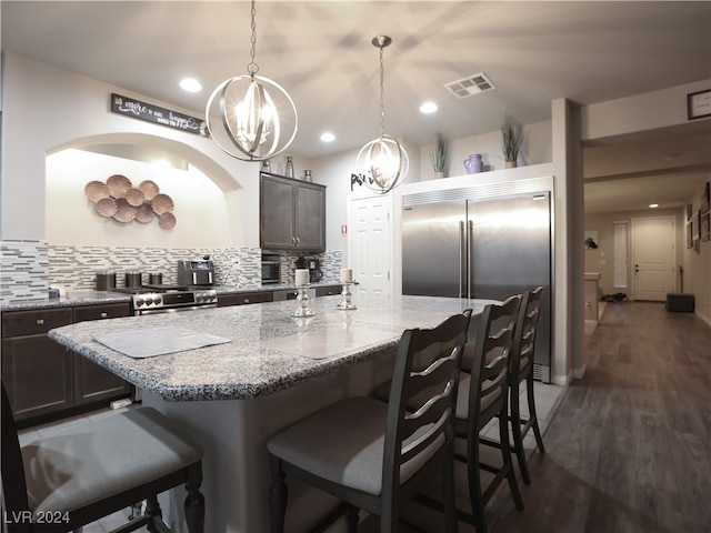 kitchen with pendant lighting, backsplash, a center island with sink, premium appliances, and dark hardwood / wood-style flooring