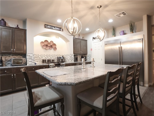 kitchen with an inviting chandelier, decorative light fixtures, decorative backsplash, a center island with sink, and high end appliances