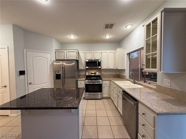 kitchen with stainless steel appliances, a kitchen island, white cabinetry, and sink