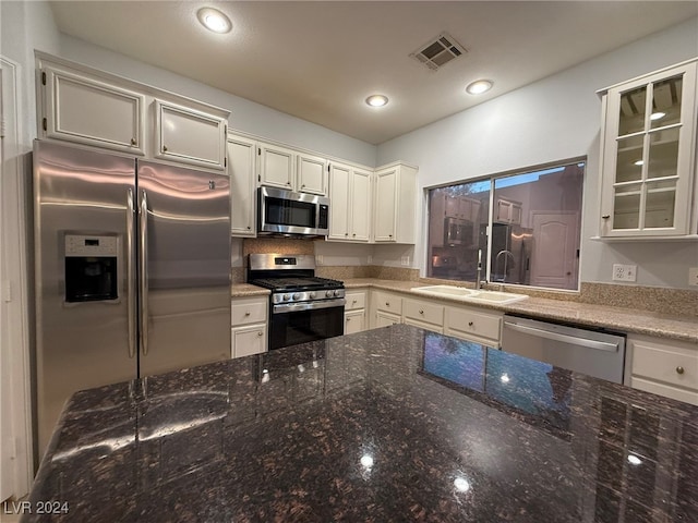 kitchen with dark stone counters, white cabinetry, sink, and stainless steel appliances