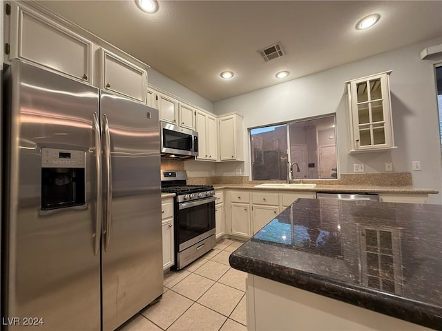 kitchen with appliances with stainless steel finishes, dark stone counters, sink, white cabinetry, and light tile patterned flooring