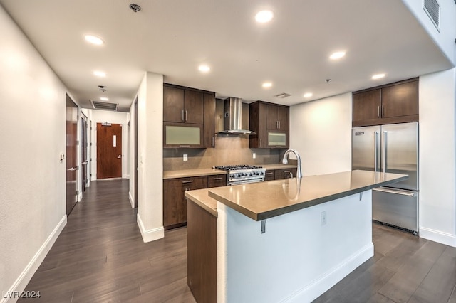 kitchen with a kitchen island with sink, wall chimney exhaust hood, dark hardwood / wood-style floors, and premium appliances