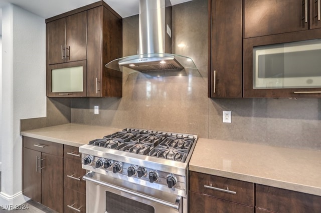 kitchen featuring high end stove, tasteful backsplash, dark brown cabinets, and wall chimney range hood