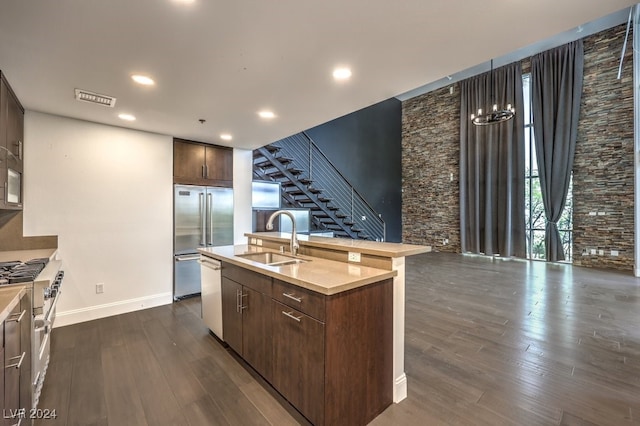 kitchen with high quality appliances, dark wood-type flooring, sink, and an island with sink