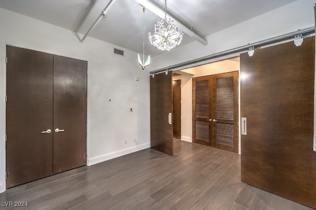 unfurnished bedroom featuring hardwood / wood-style flooring, a notable chandelier, and a barn door