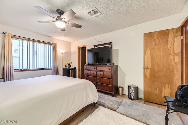 bedroom with ceiling fan, light hardwood / wood-style floors, and a textured ceiling