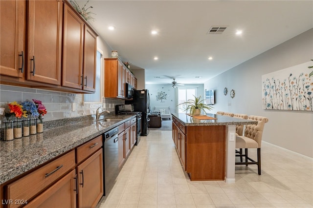 kitchen featuring a center island, dark stone counters, black appliances, a kitchen breakfast bar, and sink