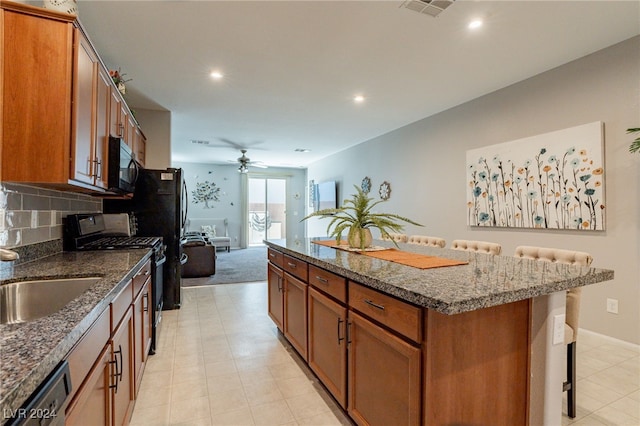 kitchen with black appliances, sink, decorative backsplash, a kitchen island, and a kitchen bar