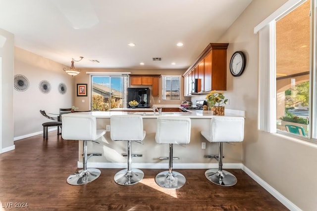 kitchen featuring black refrigerator, decorative light fixtures, dark hardwood / wood-style flooring, a kitchen breakfast bar, and stove