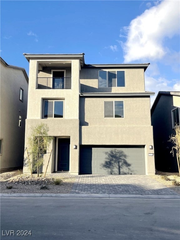 view of front of house featuring a garage, decorative driveway, a balcony, and stucco siding