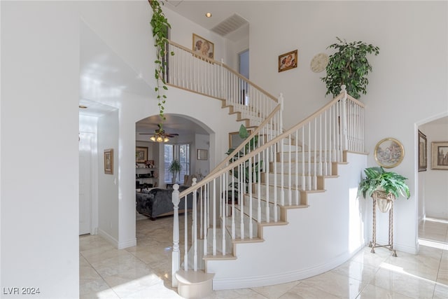 stairway featuring a towering ceiling and ceiling fan