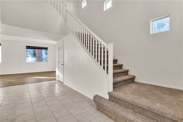 stairway featuring tile patterned floors, a healthy amount of sunlight, and a towering ceiling