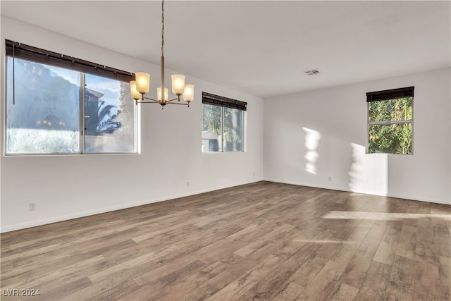 unfurnished room featuring a chandelier, a healthy amount of sunlight, and wood-type flooring