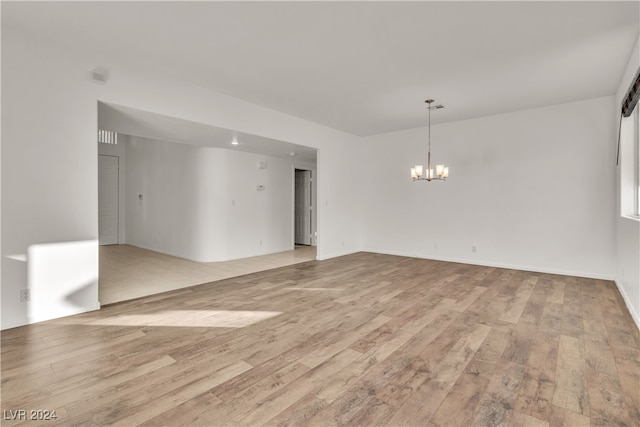 spare room with a notable chandelier and light wood-type flooring