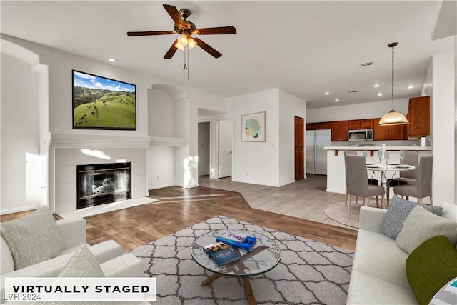 living room with a fireplace, ceiling fan, and light hardwood / wood-style flooring