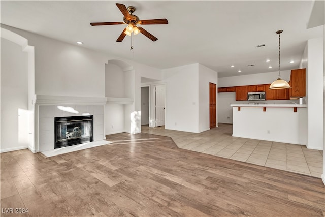 unfurnished living room with a tiled fireplace, ceiling fan, and light wood-type flooring