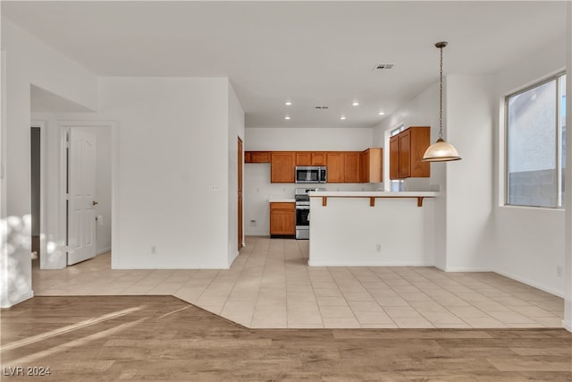 kitchen featuring hanging light fixtures, kitchen peninsula, light hardwood / wood-style floors, a breakfast bar, and appliances with stainless steel finishes