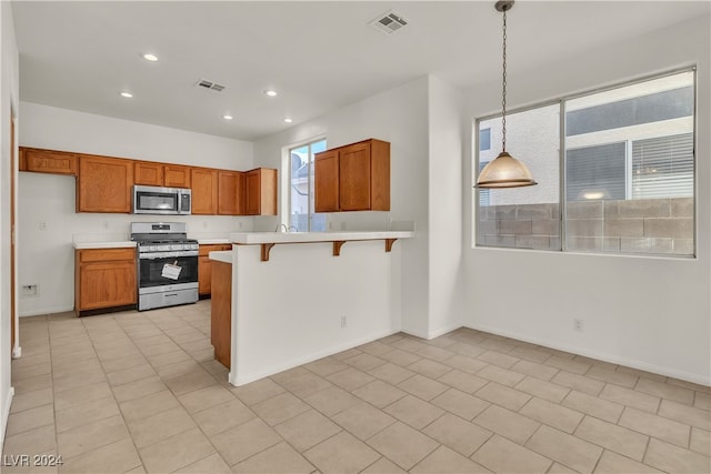 kitchen with kitchen peninsula, appliances with stainless steel finishes, a kitchen breakfast bar, light tile patterned floors, and decorative light fixtures