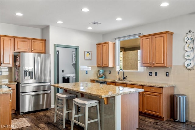 kitchen featuring washer and clothes dryer, dark hardwood / wood-style floors, a breakfast bar, a kitchen island, and appliances with stainless steel finishes