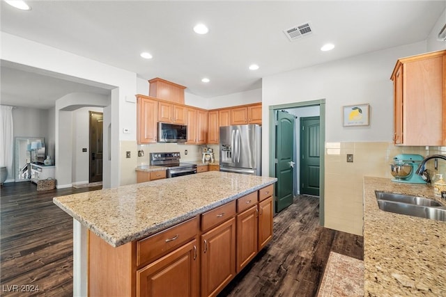 kitchen featuring sink, appliances with stainless steel finishes, light stone counters, a kitchen island, and dark wood-type flooring