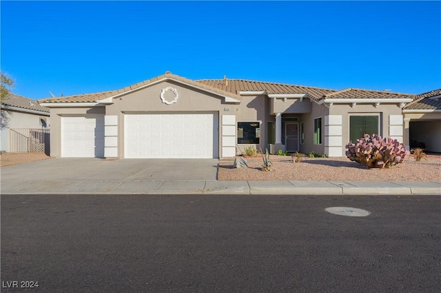 view of front facade featuring stucco siding, driveway, a tile roof, and a garage