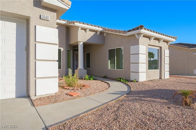 doorway to property featuring stucco siding, a tile roof, and a garage