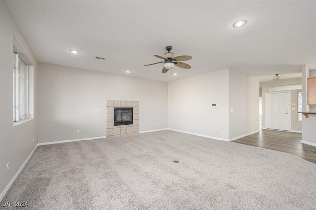 unfurnished living room with a tile fireplace, ceiling fan, and dark carpet