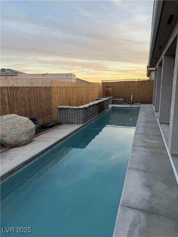 pool at dusk featuring a fenced in pool and a fenced backyard