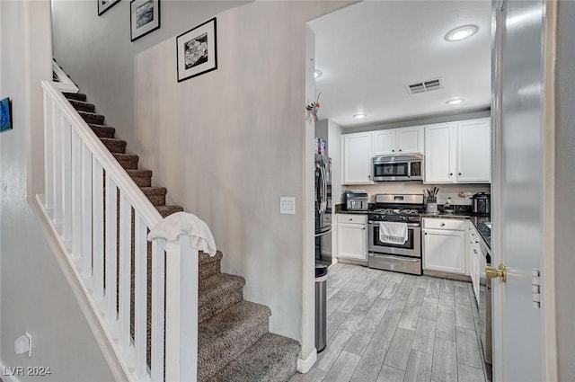 kitchen with appliances with stainless steel finishes, white cabinetry, and light hardwood / wood-style flooring