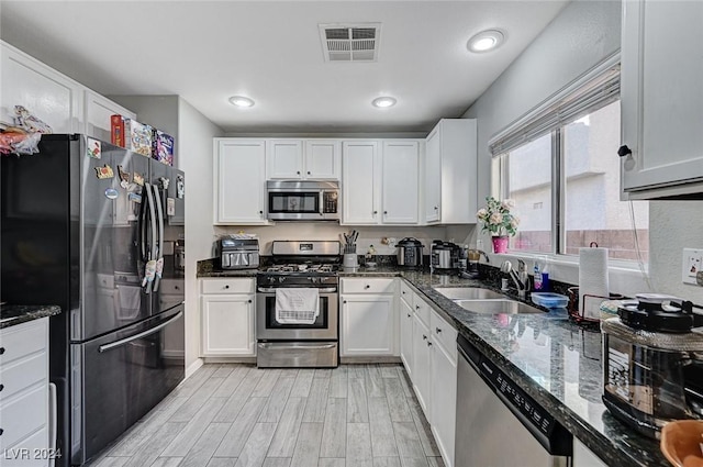 kitchen featuring sink, stainless steel appliances, dark stone countertops, light hardwood / wood-style floors, and white cabinets