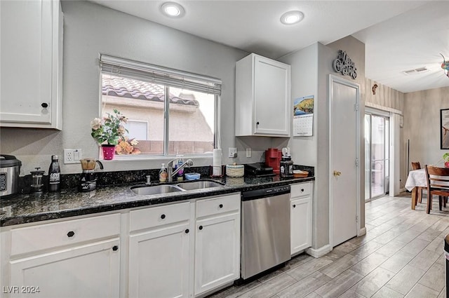 kitchen with dishwasher, dark stone counters, white cabinets, sink, and light hardwood / wood-style flooring