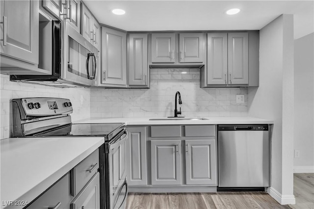 kitchen featuring gray cabinetry, sink, stainless steel appliances, decorative backsplash, and light wood-type flooring