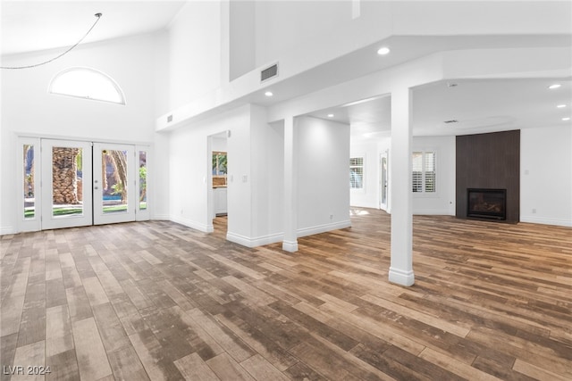 unfurnished living room with wood-type flooring, a fireplace, a high ceiling, and french doors