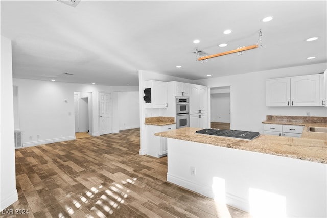 kitchen featuring gas stovetop, light stone counters, double oven, white cabinets, and hardwood / wood-style flooring