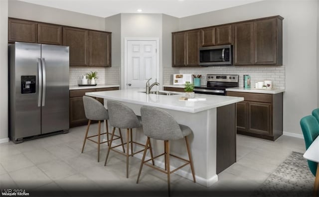 kitchen featuring sink, an island with sink, stainless steel appliances, and dark brown cabinets