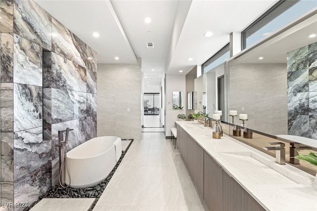 bathroom with a washtub, vanity, tile patterned floors, and tile walls