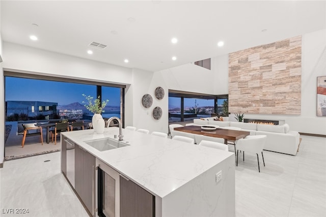 kitchen with dishwasher, light stone counters, sink, and an island with sink