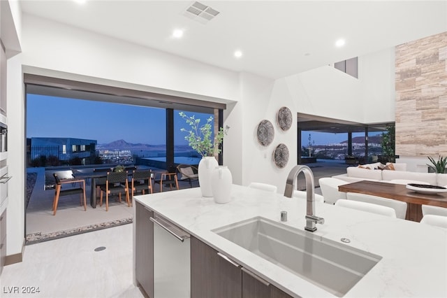 kitchen featuring dark brown cabinetry, light stone countertops, sink, and stainless steel dishwasher